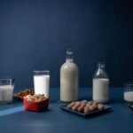 Variety of nut milks and raw nuts arranged on a table against a dark background.